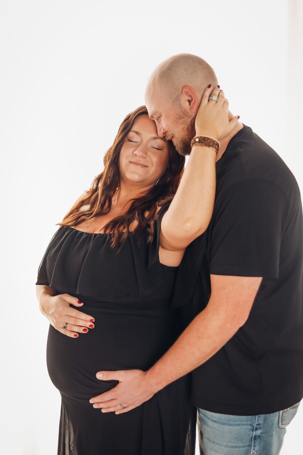 A tender maternity photo of a couple in black clothing embracing against a white background.