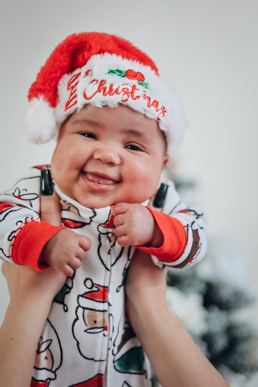 Baby wearing Santa hat and holiday outfit smiling brightly at camera. Milestone photography