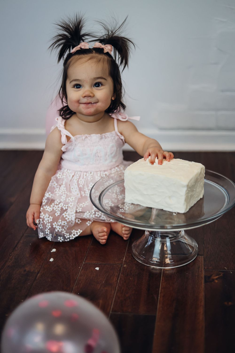 White frosted cake on glass stand against wooden surface. Cake smash studio session