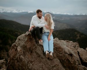 Romantic couple sitting together on rocky mountain overlook at sunset.
