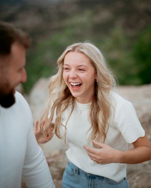 Candid moment of joyful laughter between couple in matching white tops on mountainside.