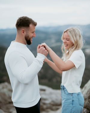 Couple in white tops holding hands and celebrating on mountain peak.