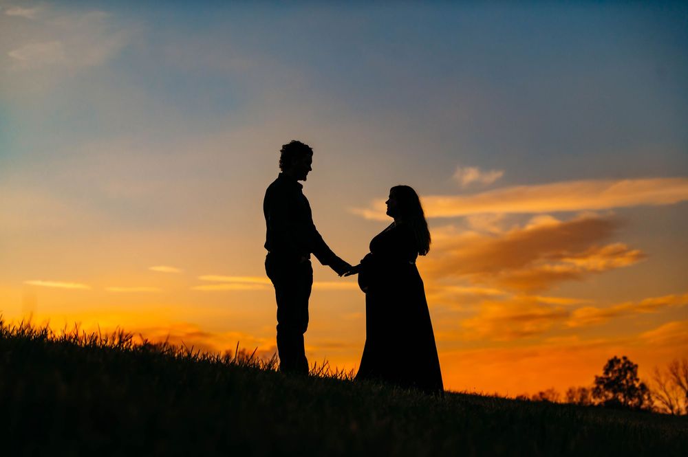 Silhouetted couple holds hands on hilltop against vibrant orange sunset sky.