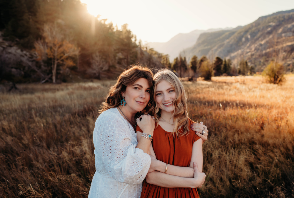 Two people in casual attire share an intimate moment at sunset in a golden mountain meadow.