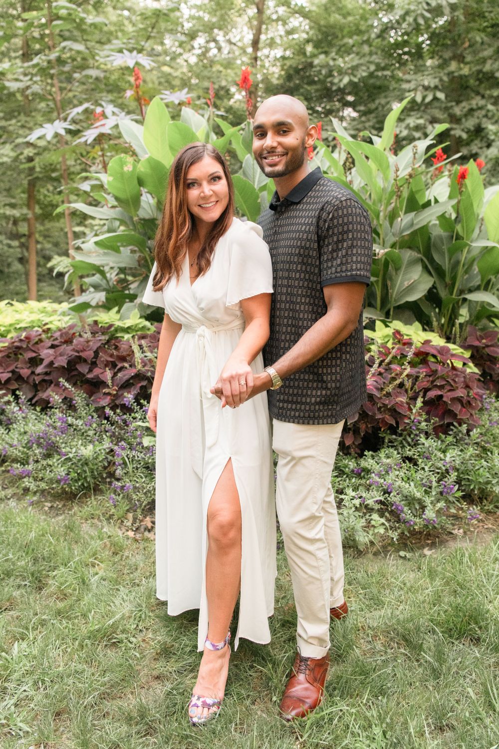 A couple stands together in a lush garden setting with tropical plants and flowers.