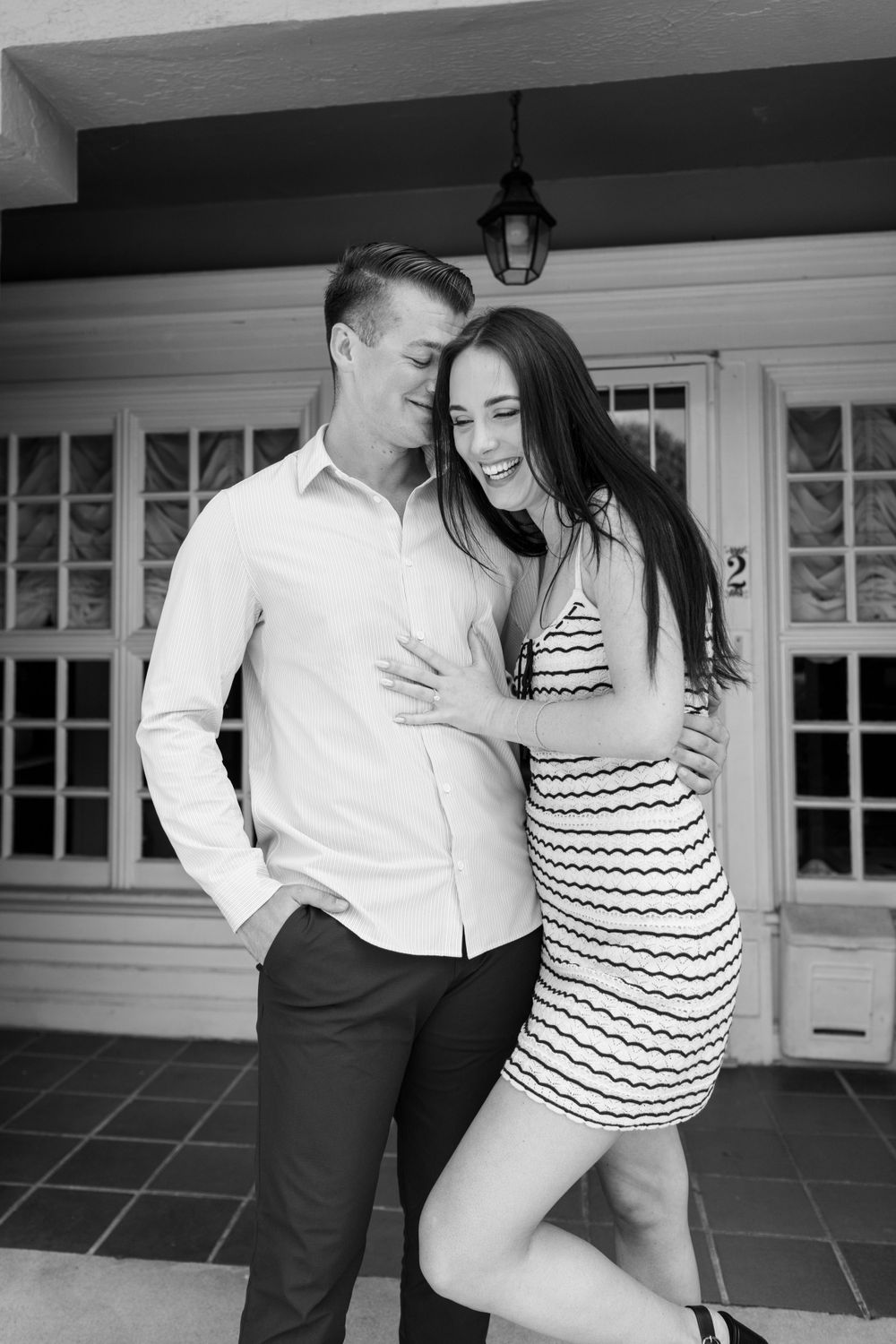 A romantic black and white portrait of a couple embracing on a porch.