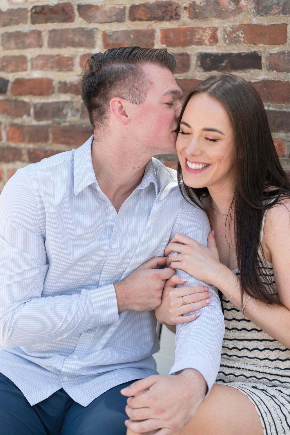 A sweet moment between a couple sitting together against a brick wall.