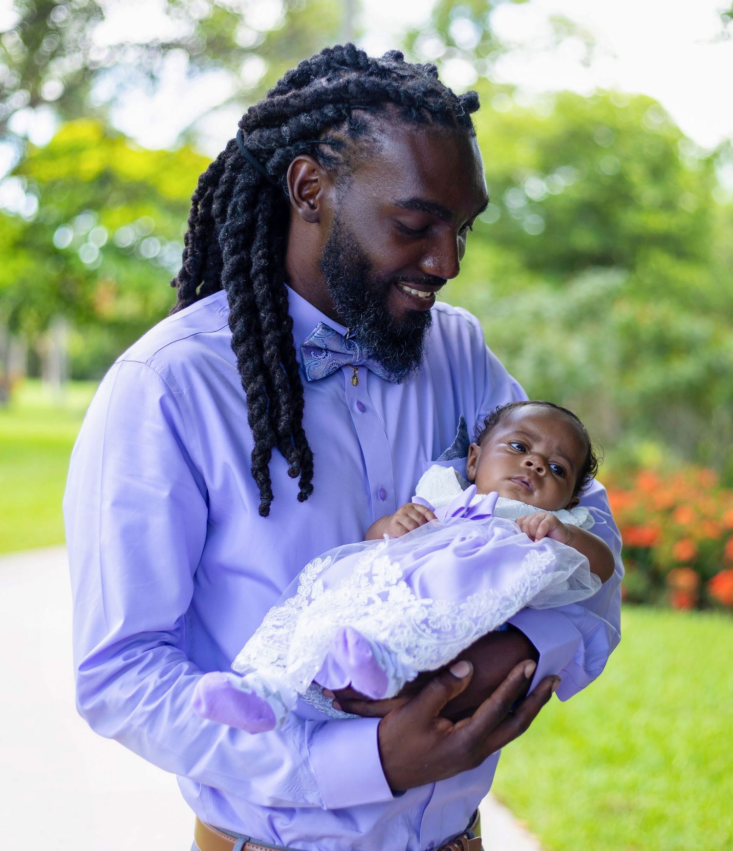 Person in purple shirt holding and bonding with infant outdoors.