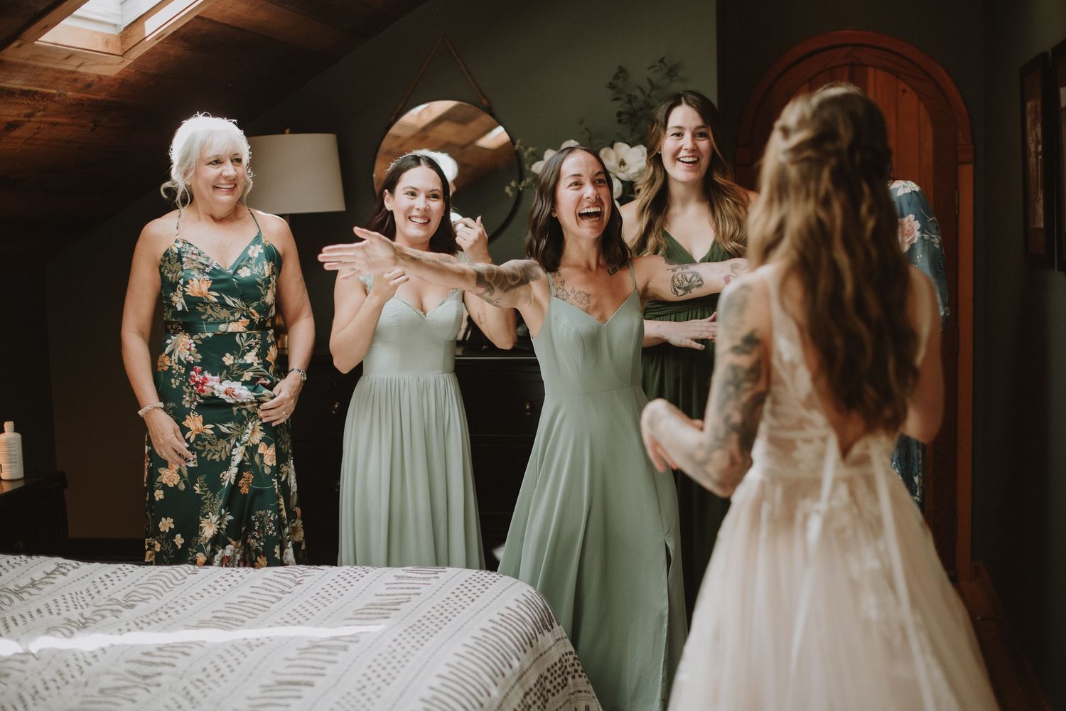 A candid moment of joyful celebration with bridesmaids in sage green dresses reacting to seeing the bride.