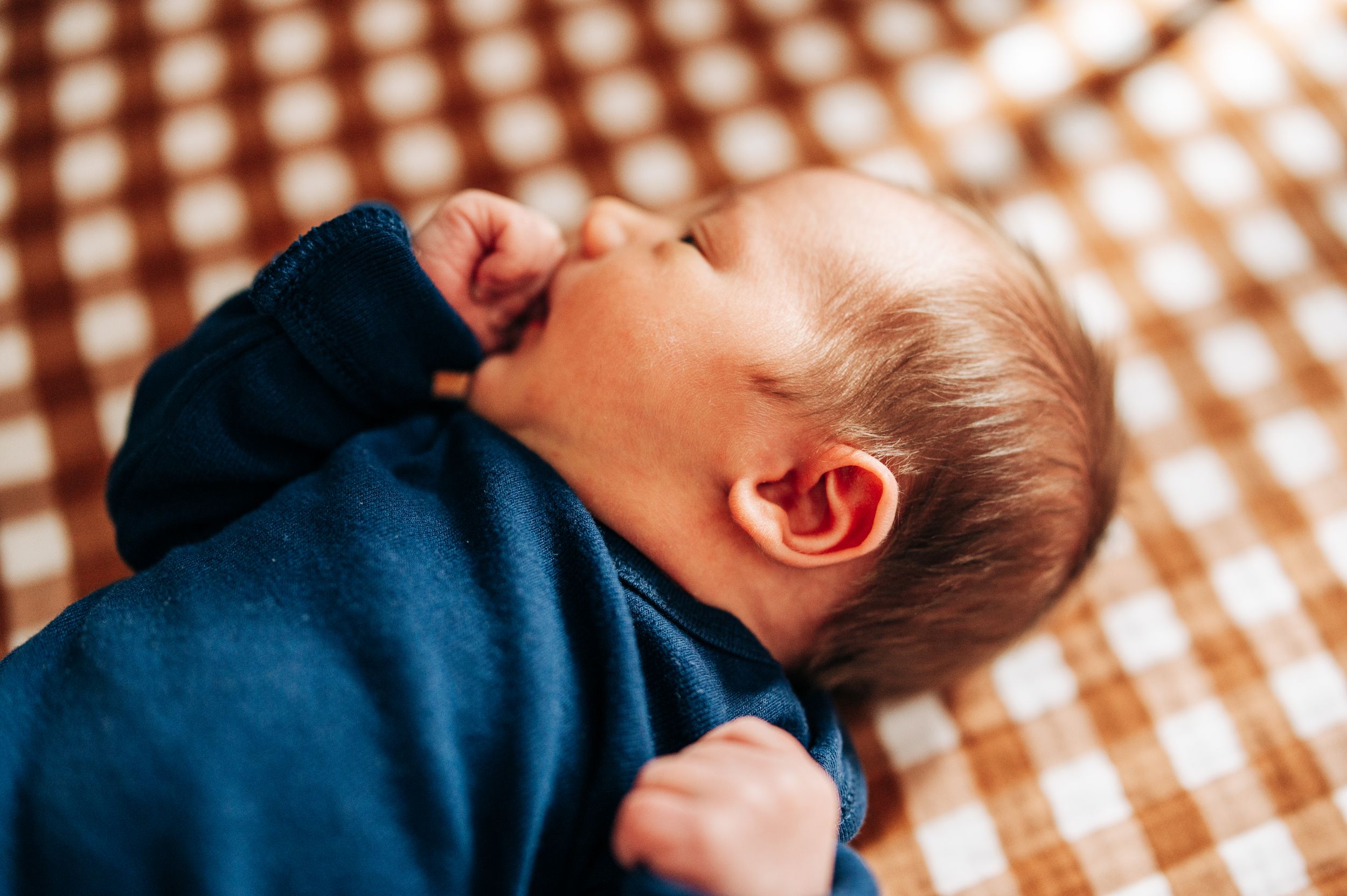 Close up of baby in navy blue outfit sleeping peacefully on checkered blanket.