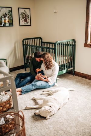 Couple sitting on floor by green crib with white dog lying nearby in nursery.