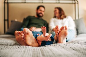 Bare feet of family members resting together on gray bedding.