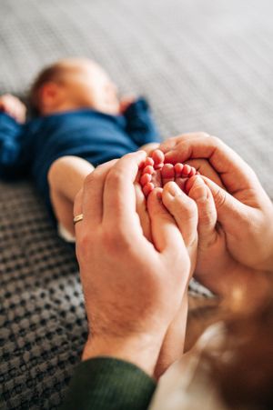 Close up of hands gently holding tiny baby feet on textured gray fabric.
