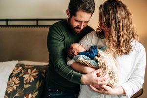 Family sharing tender moment while holding baby wrapped in knit blanket.