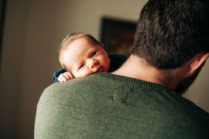 Baby smiling over shoulder while being held against green sweater.