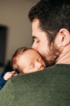 Tender moment as baby sleeps on shoulder in green sweater.