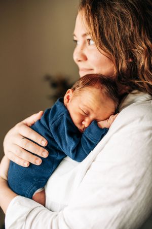 Baby in blue sleeper snuggled against white sweater during intimate moment.
