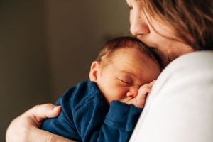 Peaceful newborn in blue outfit nestled against white clothing.