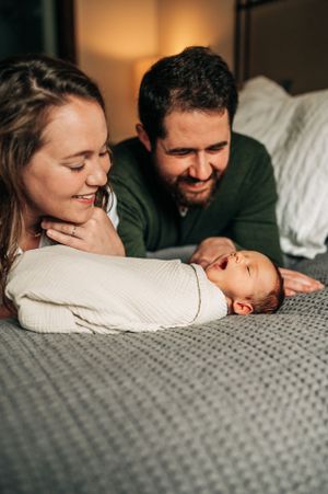 Family moment with swaddled baby lying on grey blanket.