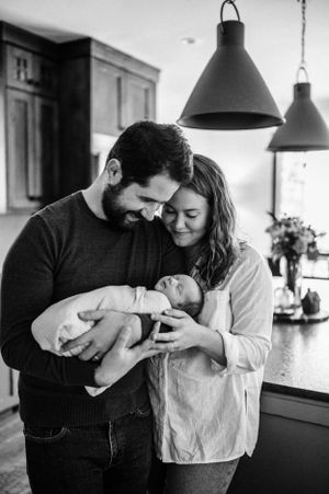 Intimate black and white portrait of a family with newborn baby in a modern kitchen setting.