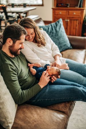 Tender family moment on a brown leather couch with a sleeping infant.