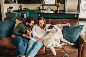 Family relaxing on couch with white dog and baby in casual home setting.
