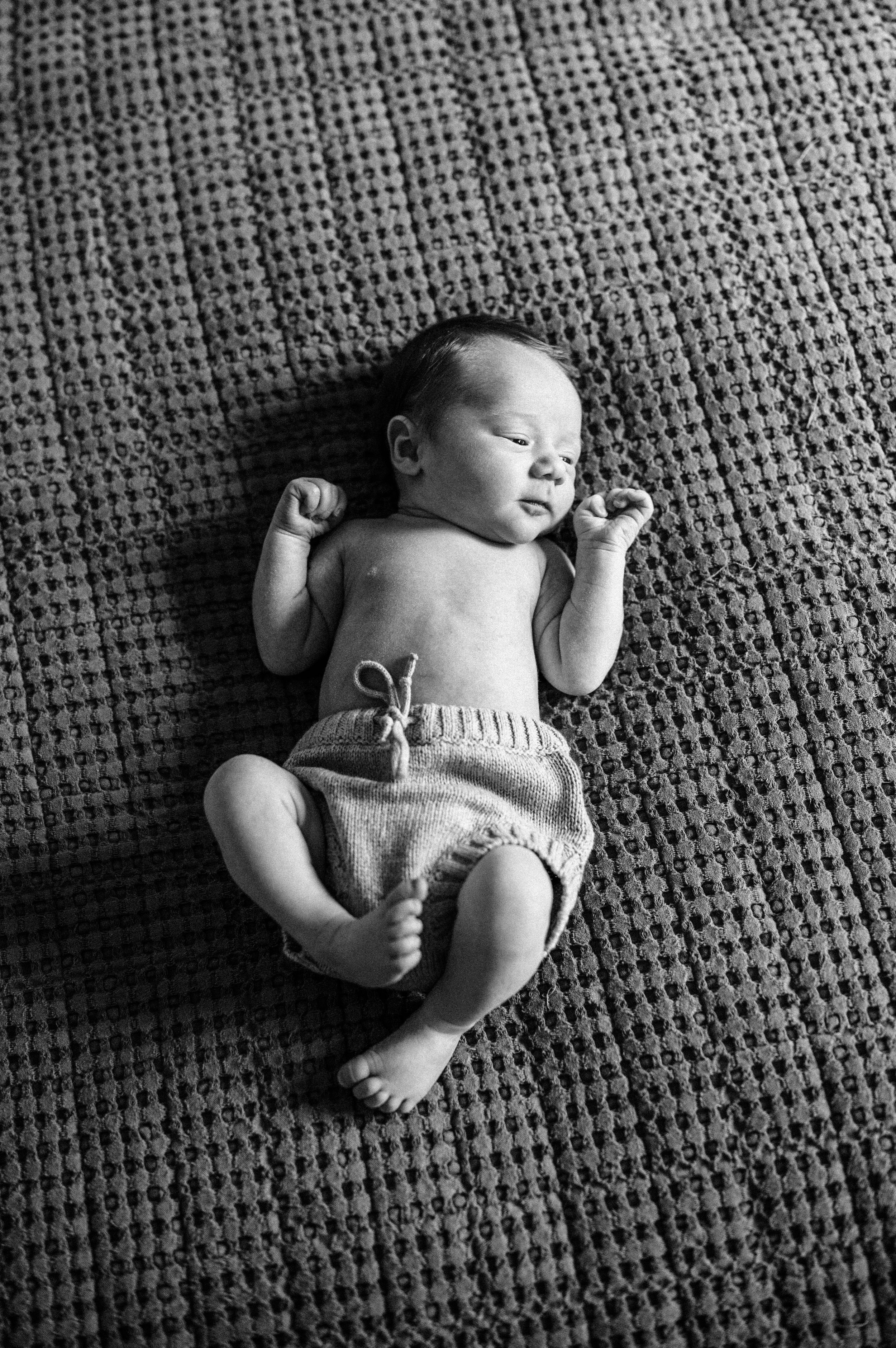 Black and white portrait of sleeping newborn baby on textured blanket.