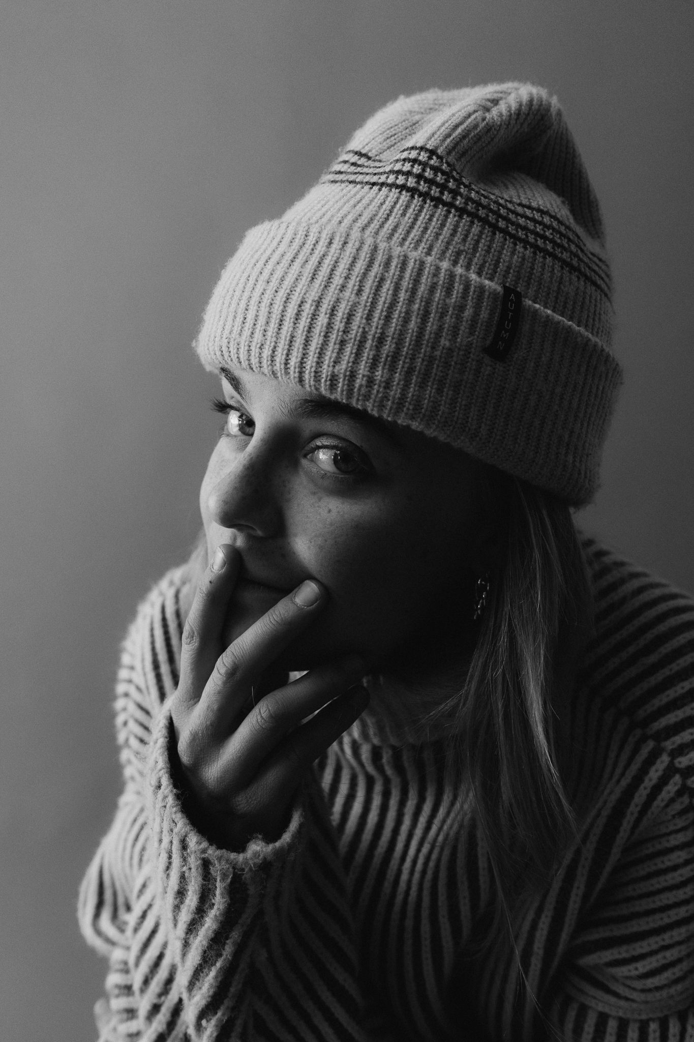 Dramatic black and white close-up portraits showing person in winter hat and turtleneck.