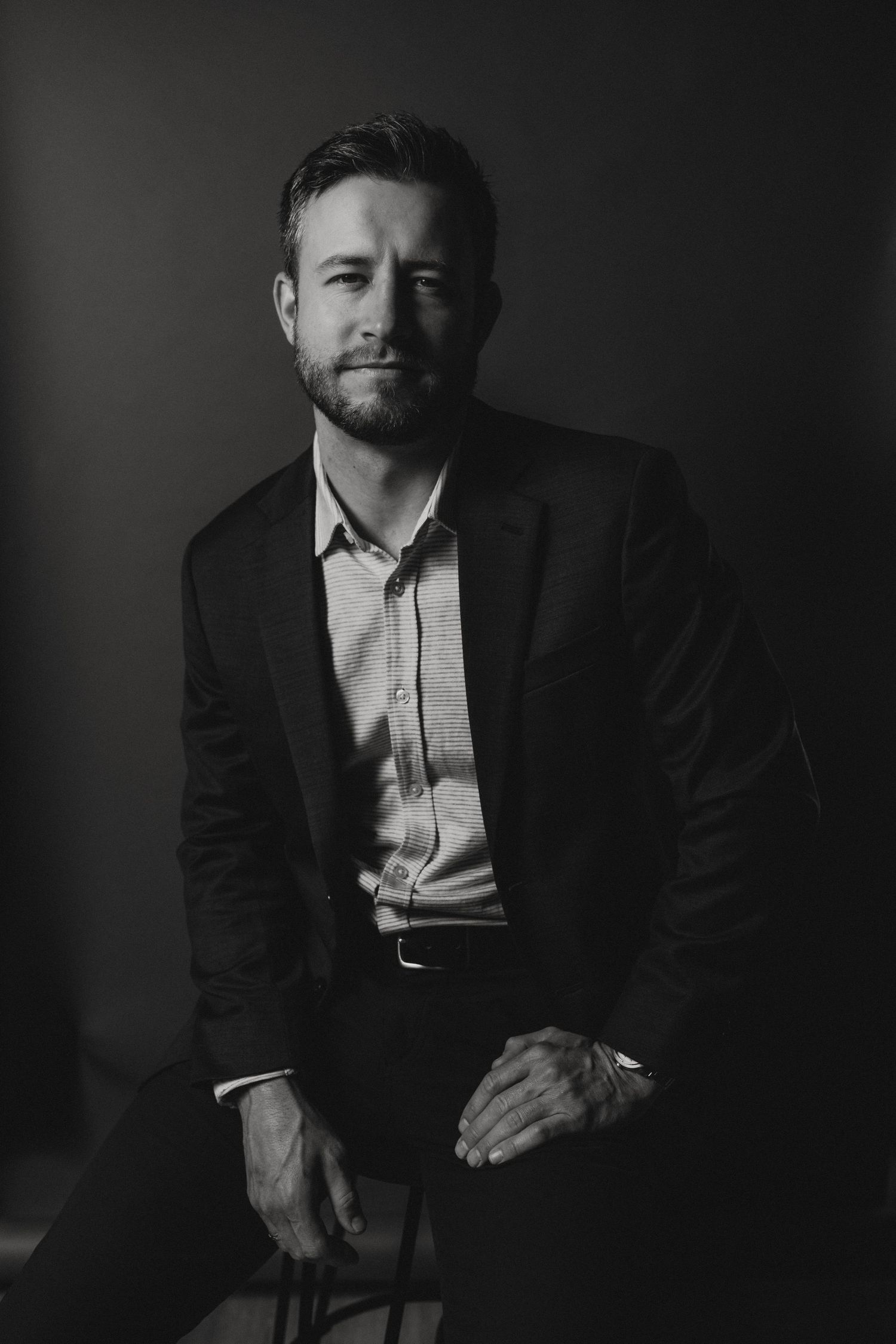 Dramatic black and white portrait series of someone in a suit sitting against dark background.
