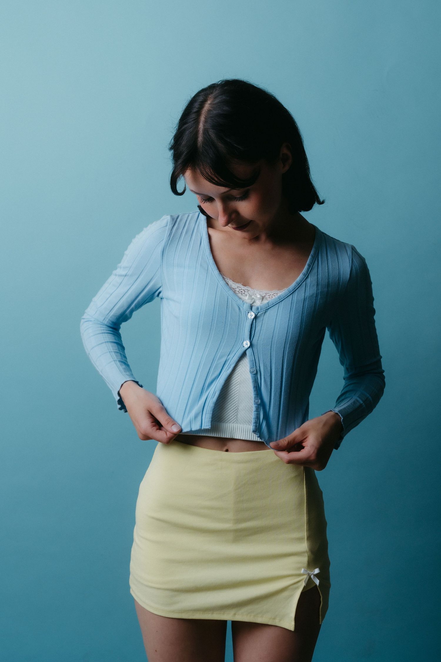 Fashion sequence showing person in light blue top and beige skirt against turquoise background.