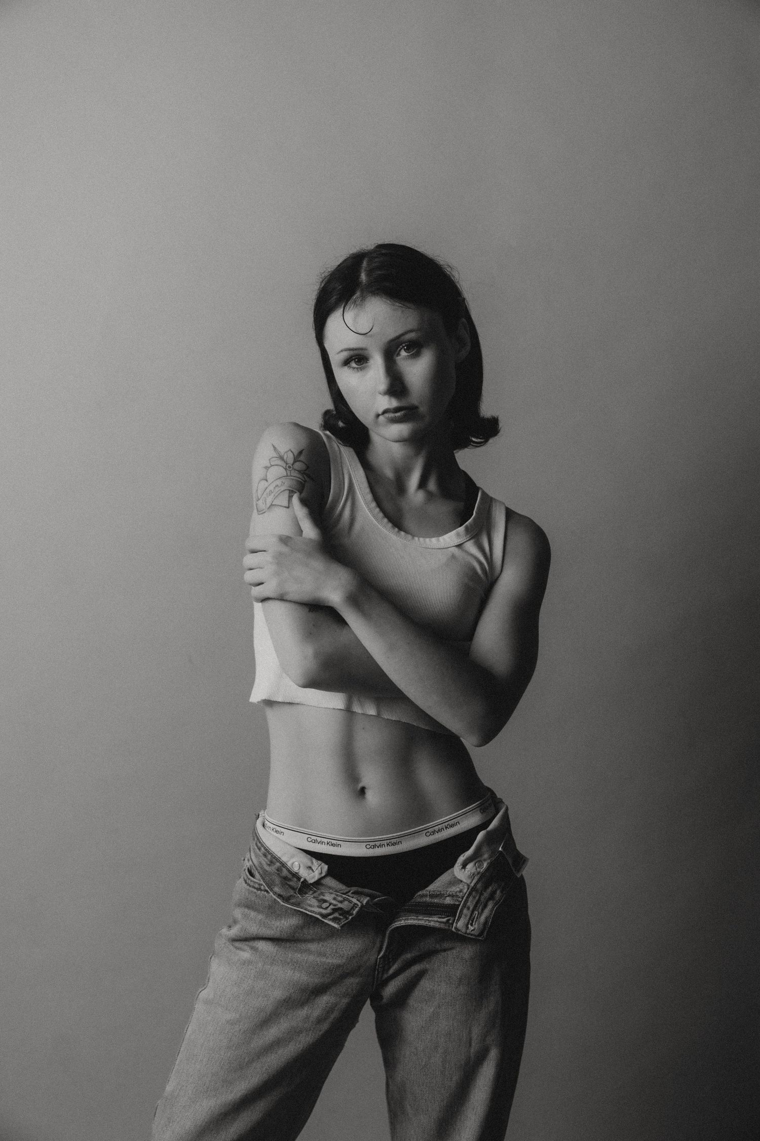 Black and white artistic photo series showing poses in casual jeans and cropped top against a gray backdrop.