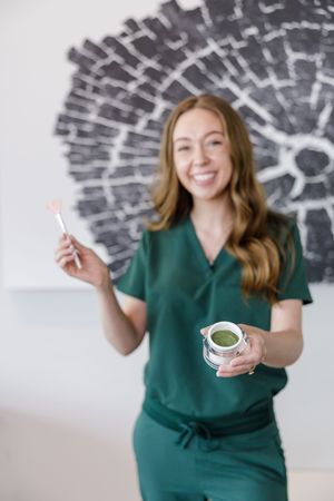 esthetician holding jar of facial mask product with a brush in foreground in hand in seattle, wA
