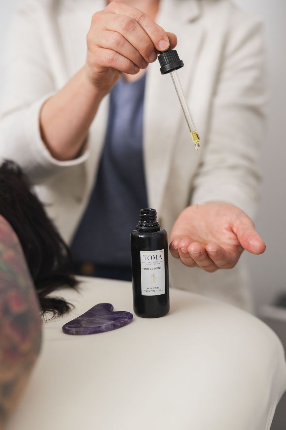 Maple Valley Acupuncture product photo of oil for gua sha on face woman using dropper of oil in hand