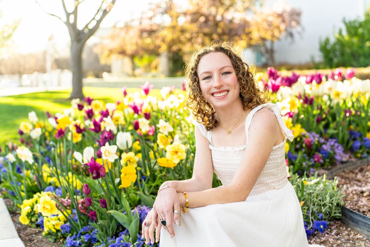 A woman in a white dress poses in a garden filled with colorful tulips and daffodils at mount timpanogos temple in American Fork, Utah.