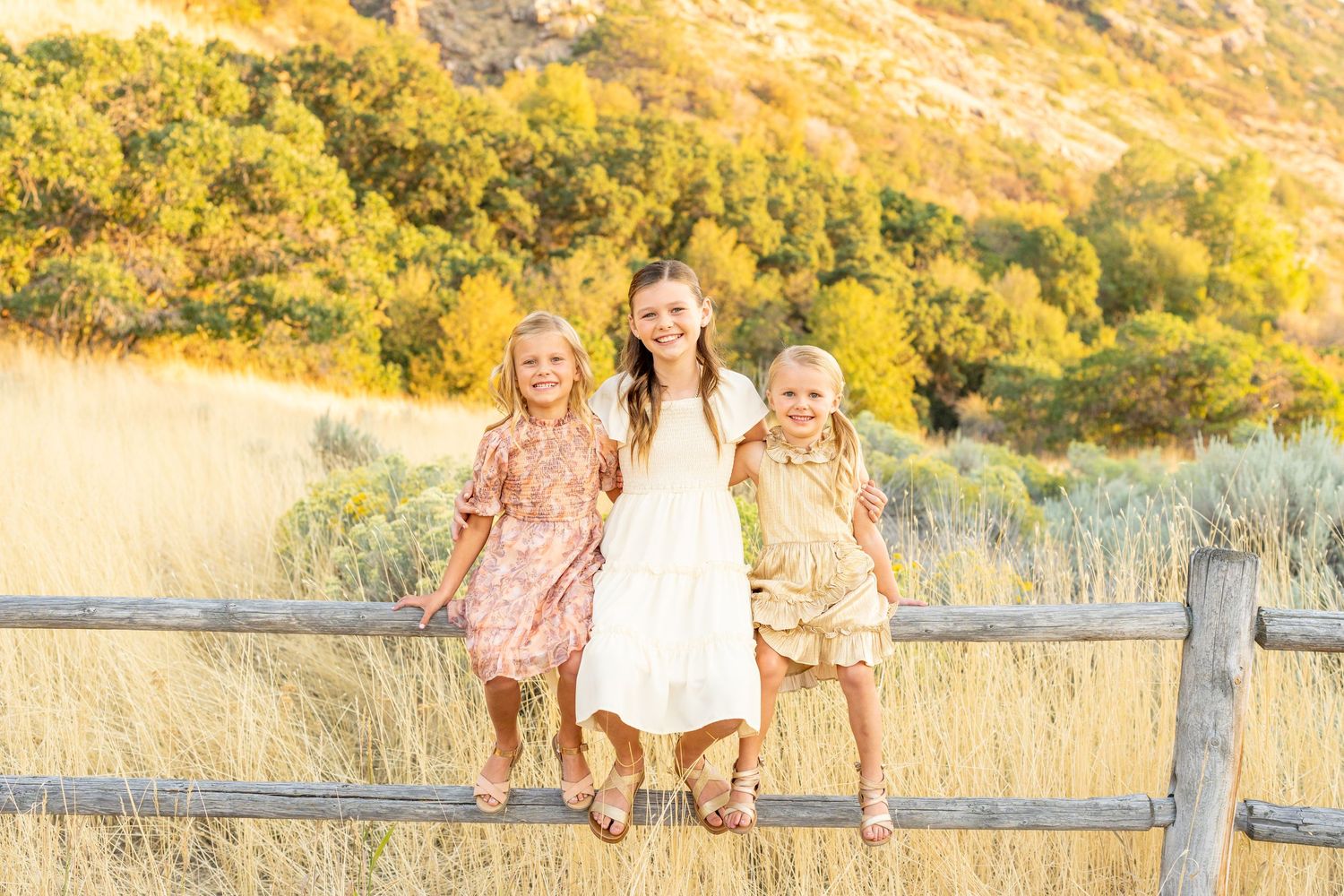 Three people sit on a wooden fence with golden hills in the background at Hidden Valley Park, Utah.