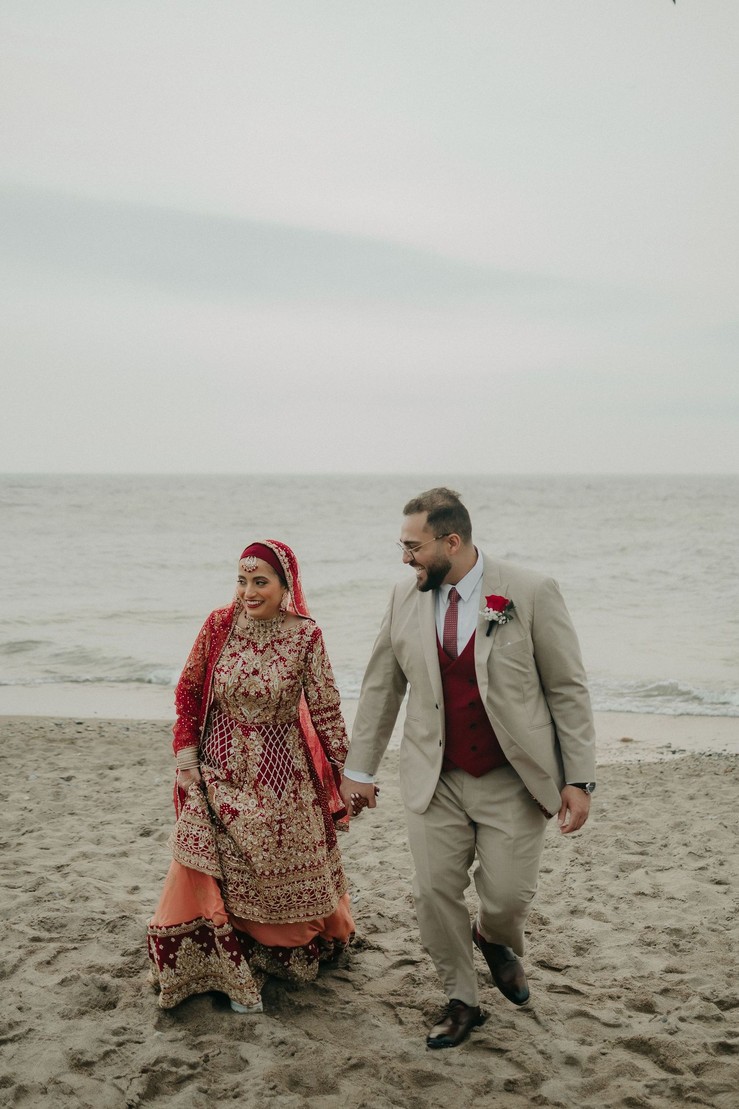 A couple in wedding attire taking a romantic walk along a misty beach.