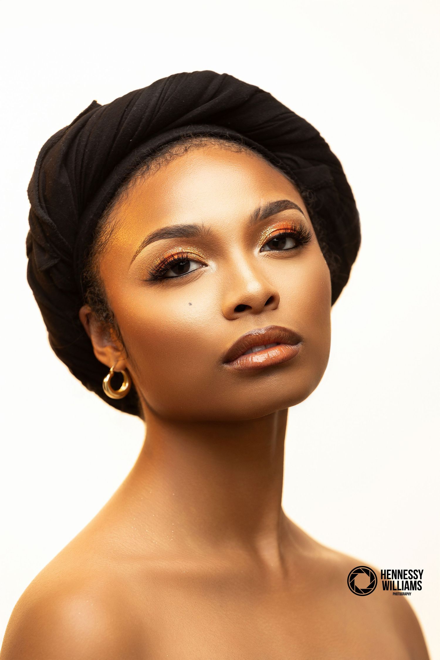 Professional beauty portrait with sleek black t-shirt, dark lipstick, and elegant makeup against a brown backdrop.