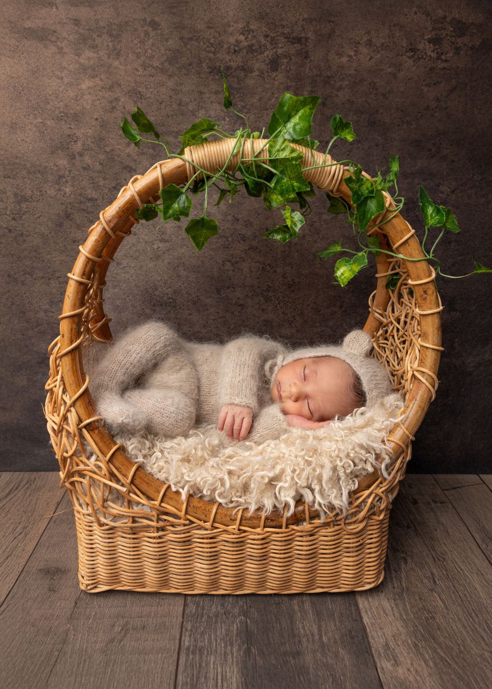Sleeping baby nestled in a rustic woven basket adorned with delicate lace and greenery against a dark backdrop.
