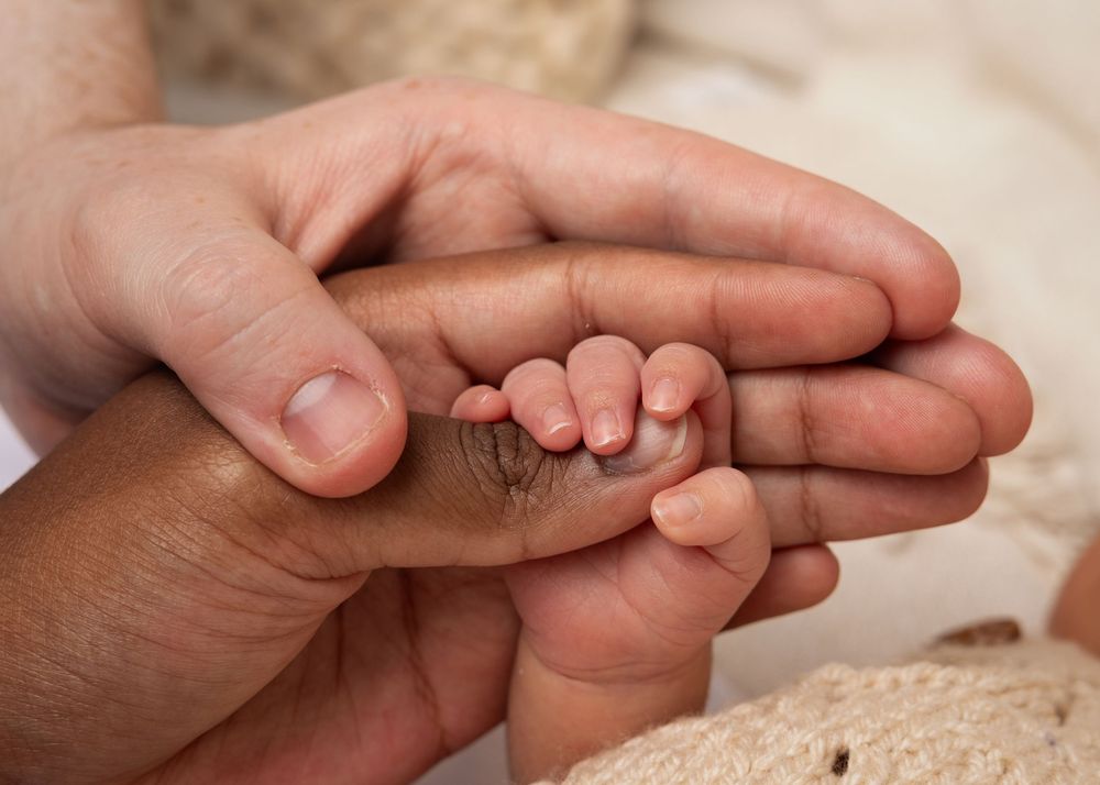 Four close-up photos showing gentle hands holding tiny baby feet against a soft cream background.