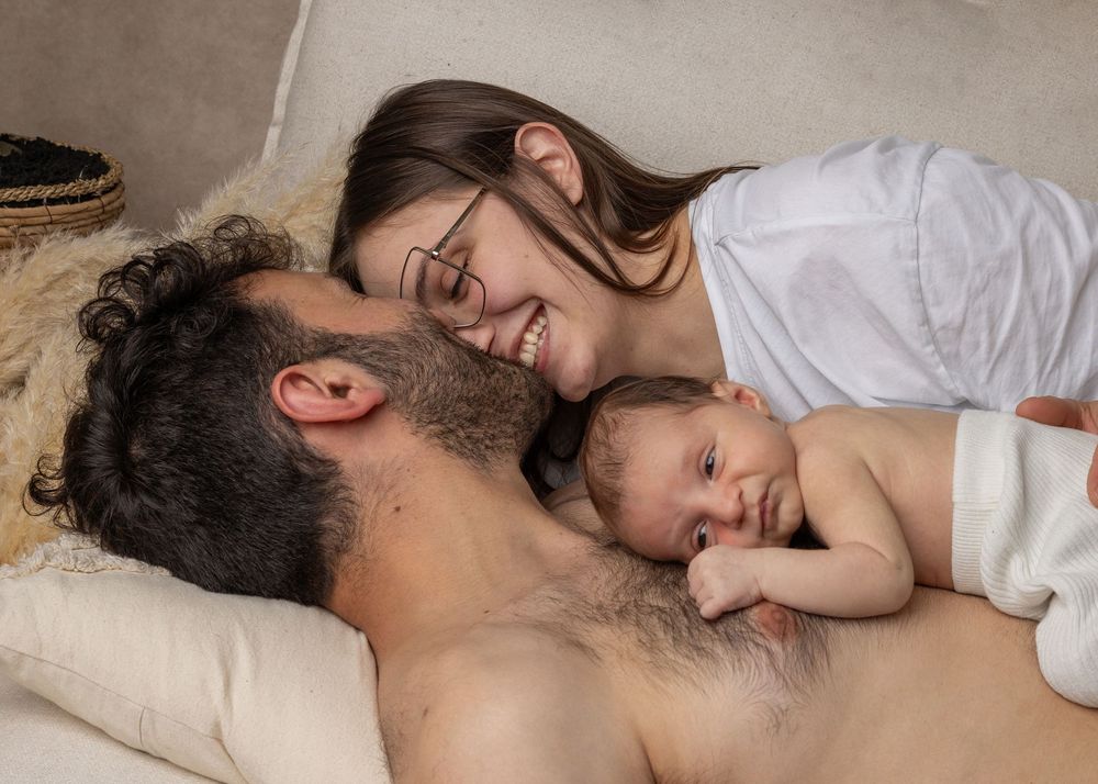 A tender family moment shows a sleeping infant resting peacefully on a caregiver's chest while reclining on pillows.