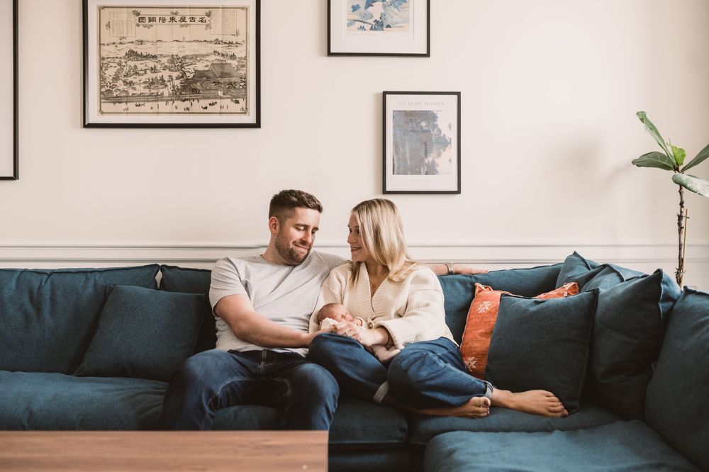 Couple with their newborn baby relaxing together on a comfortable blue couch in a modern living room interior.