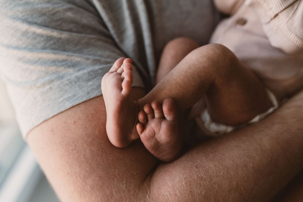 A close-up shot of a newborn baby's feet on her father's arms.