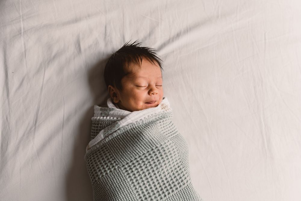A newborn baby sleeps peacefully wrapped in a soft gray knitted blanket during a newborn photo session.