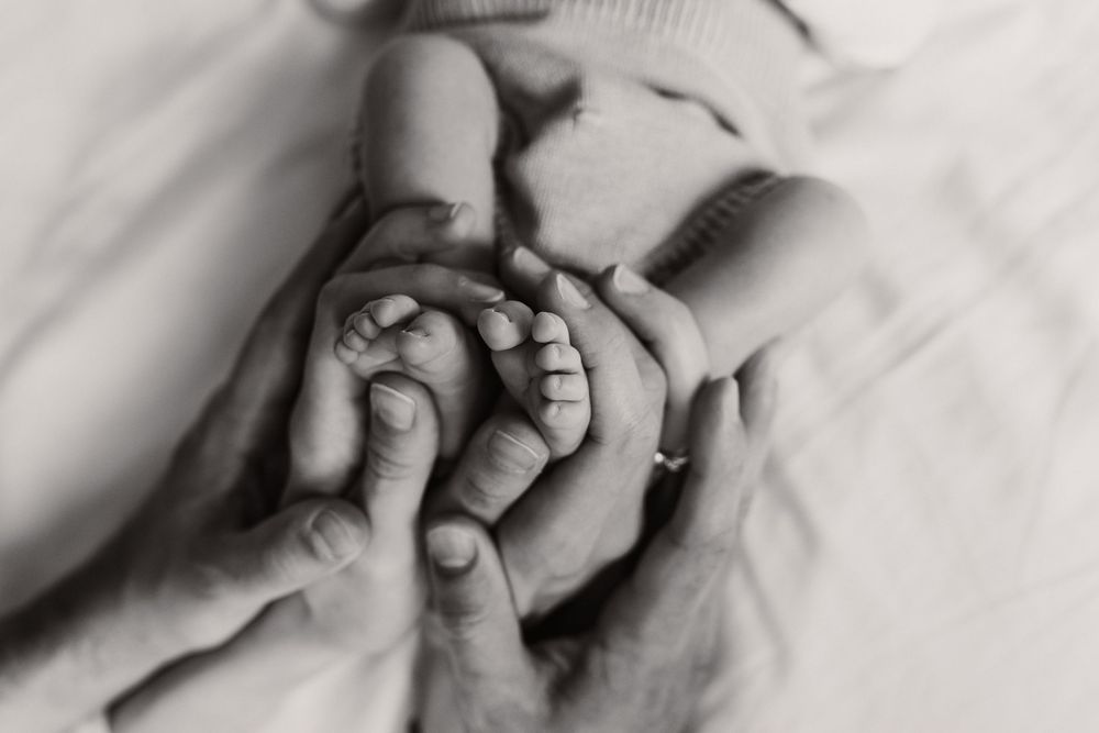Black and white close-up image of hands gently holding a newborn baby's tiny feet.