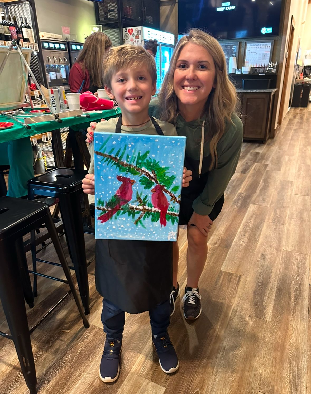 Colorful painting of red cardinals on snowy branches displayed in art studio setting.