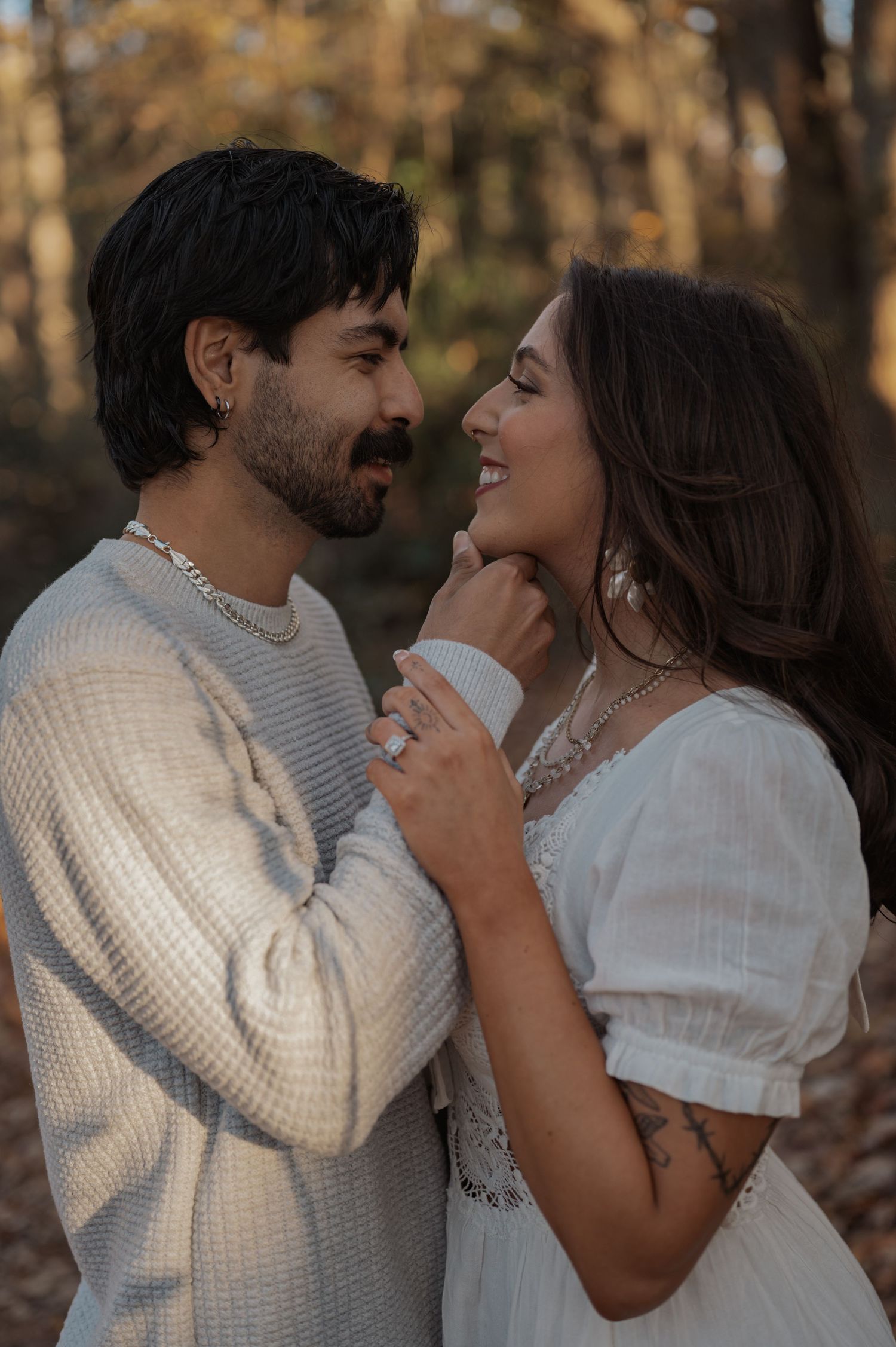 A couple in white clothing shares a romantic moment in autumn woods during golden hour.