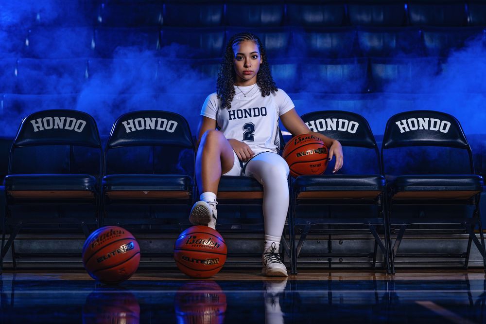 Basketball player holds ball while sitting on bench in empty arena with blue lighting.