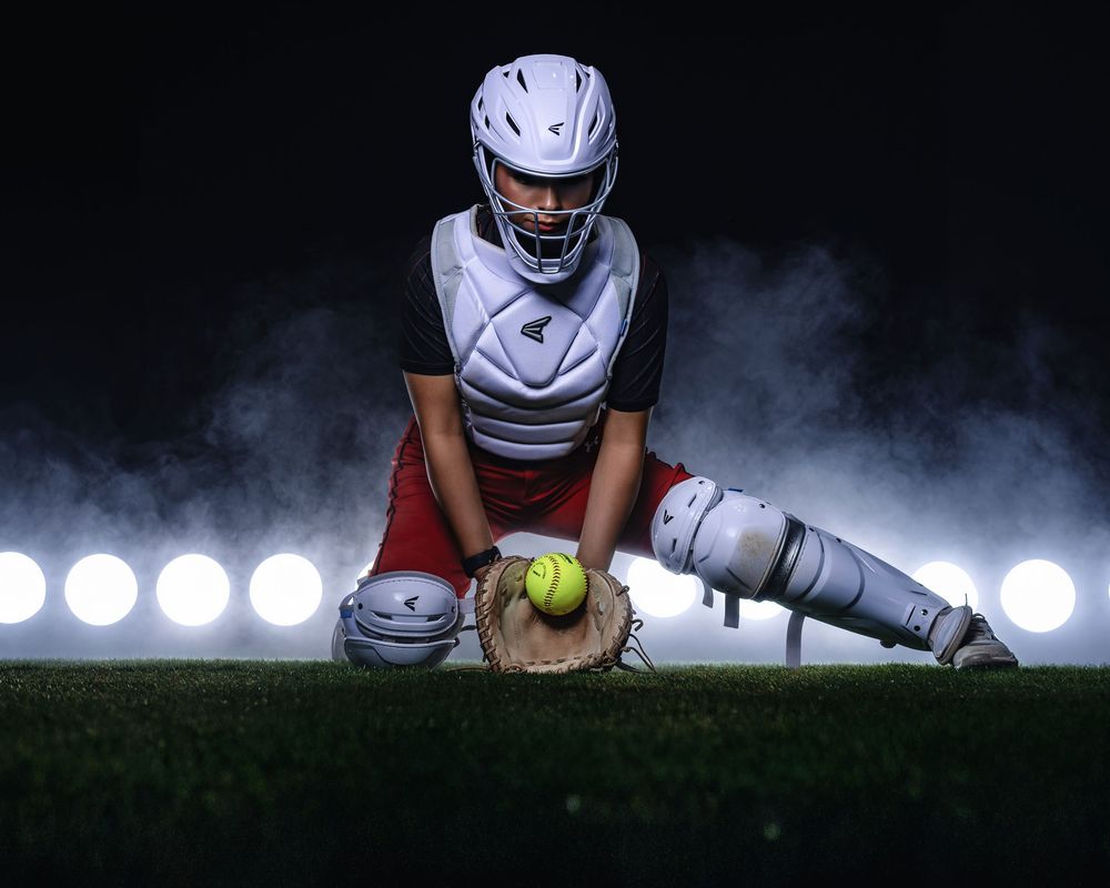 A softball player in white uniform slides into base with dramatic lighting and smoke effects in the background.