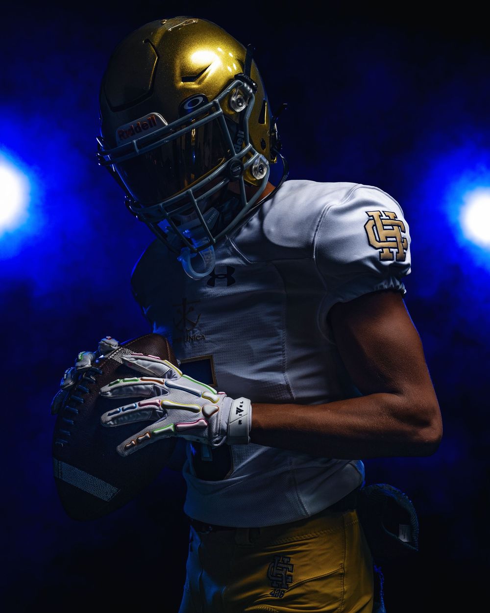 Football player in white jersey and gold helmet shown in dramatic blue lighting with silhouette effect.