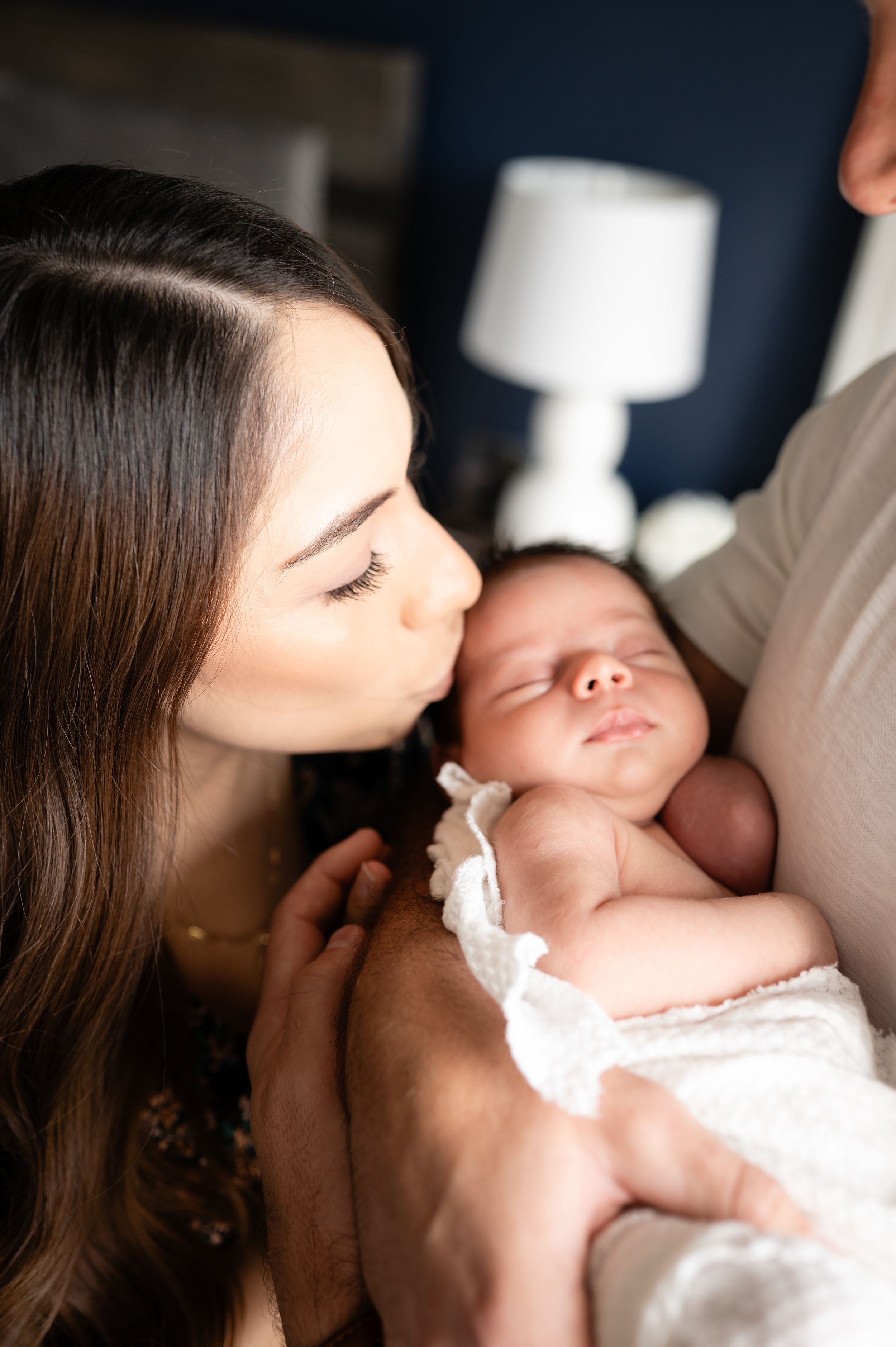 Tender moment with swaddled newborn in white against dark background.